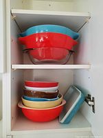 Stacked Pyrex bowls of red, blue, and clear glass inside cabinet shelf