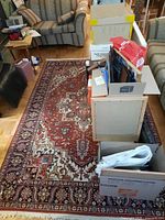 Full view of rug under stacked boxes and furniture showing overall condition and approximate full dimensions.