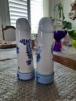 Pair of tall white ceramic salt and pepper shakers decorated with blue hand painted designs viewed from the back side.