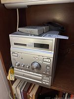 Front view of the Sony micro hi-fi system with cassette deck and control panel showing knobs and buttons. Two remote controls placed on top.