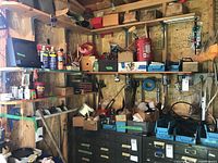 Wide view of shed shelving with various tools and hardware including cans, boxes, tools, and storage drawers