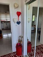 Red ceramic umbrella stand with two umbrellas inside, showing crack on stand.