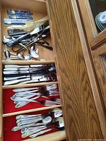 Drawer with multiple compartments containing assorted utensils including forks, knives, spoons, tongs.