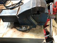 Side angle view of the vise showing the handle, jaws, and mounting base with dirt and rust.