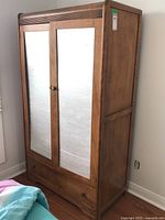 Side and angled view of wooden wardrobe cabinet with silver painted panels on doors, two doors, and bottom drawer.