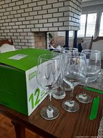 Photo showing a set of 12 Everyday Essentials versatile wine glasses in their original box along with some clear stemmed glasses on table.
