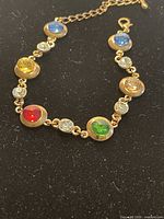 Colorful gemstone brass link bracelet showing multicolored stones set in round bezels connected by small clear rhinestones.