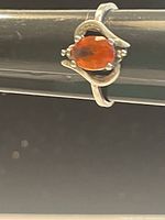 Close-up view of a sterling silver ring with an oval faceted orange gemstone, showing the front design and band details.