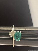 Close-up image of ring showing oval green gemstone and a smaller clear gemstone on a polished 925 silver band.