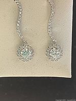 Pair of drop earrings featuring sparkling Swarovski crystal clusters and curved crystal-encrusted hooks displayed on a light fabric background.