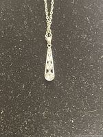 Front view of necklace pendant with three Swarovski crystals in teardrop setting on silver chain against a black background