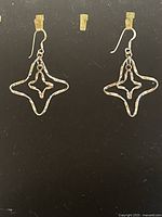 Pair of .925 sterling silver dangle earrings with geometric star-shaped hollow design on black background.