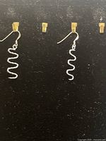 Pair of .925 sterling silver wavy dangle earrings hanging on display hooks against a black background, showing their shape and design.