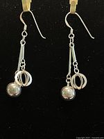 Front view of the pair of sterling silver drop earrings with spheres and rings on a black background.