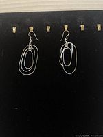 Pair of .925 sterling silver dangle earrings displayed on a black velvet earring holder. Each earring has three overlapping oval loops and hook backs.