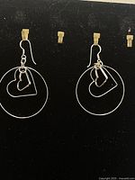 Full view of both earrings hanging on a black display, showing their large hoop shape with two heart shapes within each hoop.