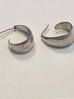 Pair of silver crescent-shaped hoop earrings with post backs, positioned side by side against a plain background.