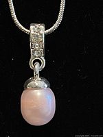 Close-up photo of the pendant showing the pink pearl and the silver bail with clear stones