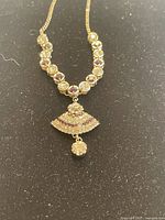 Gold-toned crystal embedded chain necklace with fan-shaped pendant and dangling round crystal displayed on black background