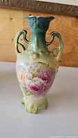 Front view of vase showing floral hand-painted design with pink roses on gradient green to yellow porcelain base and double handles