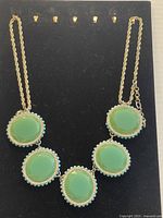 Full view of vibrant statement necklace showing five large green faceted oval stones each surrounded by turquoise beads and clear rhinestones on gold-tone chain.