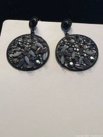 Front view of one earring showing black open filigree loop with rainbow reflective stones and solid black stud