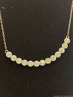 Full necklace showing curved row of rhinestones and brass chain on black background