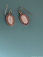 Two oval cluster crystal earrings with bronze-toned metal and clear Swarovski crystals, shown side by side on a teal background.