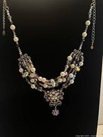 Full view of the multi-strand necklace showing beads, pearls, and floral pendant on black background.