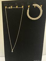 Full display black board showing the crystal cuff bracelet and the silver chain necklace with blue charm hung separately.