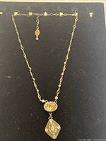 Full view of gold-tone crystal chain necklace laid on black background showing overall design with central oval champagne crystal and hanging diamond-shaped pendant.