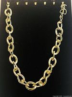 Full view of gold plated chain necklace on black background showing large oval links and two crystal encrusted links.