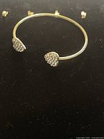 Gold plated bangle with crystal-embellished heart ends on black background.