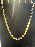 Gold plated bracelet with linked heart-shaped design displayed on a black background in a close-up view.