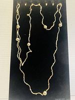 Full view of the gold plated long chain necklace displayed on a black background showing length and bead details.