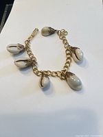 Gold plated bracelet with five cowrie shell charms, shown laid flat on white background to display details of chain, shells, and clasp.