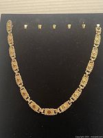 Full view of gold plated chain necklace displayed on black background with clasps in a row above the necklace.