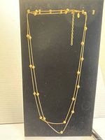 Photo of gold plated long chain necklace hanging vertically on black background showing two connected strands with small round beads spaced evenly.