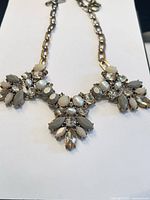 Full view of the gold-tone chain necklace showing three floral clusters of rhinestones, pearl-like beads and beige gemstones.