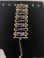 Top view of bracelet laid flat showing purple and clear crystals in gold-tone rectangular filigree frames with chain and bar clasp.