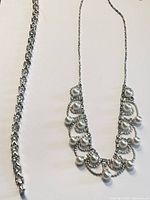 Photo showing silver-tone faux pearl necklace and silver-tone clear crystal bracelet laid flat on white background.