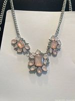 Silver-tone chain necklace with pink moonstone-like and clear rhinestone clusters, displayed on black background.