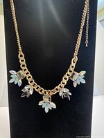 Front view of gold-tone chain necklace with rainbow crystal and moonstone decorative clusters on a black background.