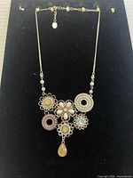 Front view of ornate bohemian necklace showing six detailed pendants including floral and circular motifs with pastel stones, filigree metalwork, and a teardrop gemstone.