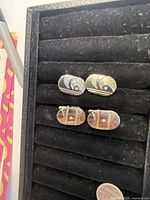 Two pairs of vintage 1970s cuff links displayed on black velvet-lined holder, showing overall condition and design details.