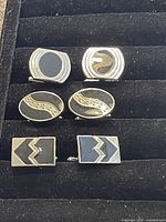 Photo of six vintage 1970s men's cufflinks arranged in two rows on a black velvet surface showing three pairs with distinct black and gold designs.
