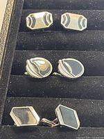 Front view of three pairs of vintage cufflinks arranged vertically in a black display case, showing their size and detailing.