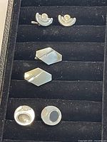 Four pairs of vintage 1970s cuff links on black velvet display, showing varied geometric and circular designs with metal, enamel, and mother-of-pearl finishes.