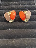 Front view of both vintage 1970s clip-on earrings with oval colored stones and floral accents on a black jewelry tray.