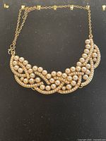 Gold-toned cluster necklace with multiple faux pearls and rhinestones on black background, showing front decorative section and chain.